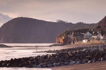 South Devon coast in the city of Sidmouth. One can see people walking on the beach. Big breakwaters from boulders. UK