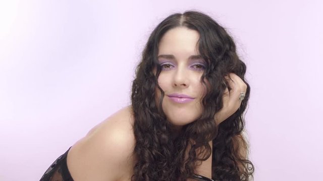 black curly hair plus size model with brown eyes poses in lilac background