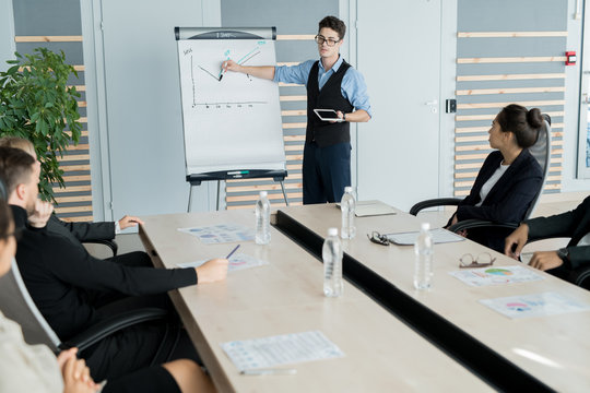 Serious confident young male business analyst in glasses holding tablet standing at whiteboard and drawing graph at meeting - Powered by Adobe