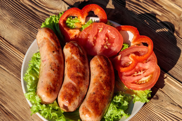 Grilled sausages with fresh vegetables on wooden table