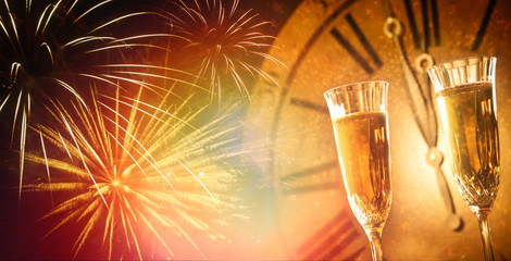 Champagne glasses against holiday lights and clock close at midnight