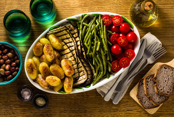 a side dish of vegetables on the holiday table. healthy food for the whole family or dinner at a restaurant on a wooden table. baked potatoes, grilled eggplants, cherry tomato salad 