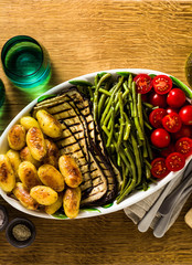 a side dish of vegetables on the holiday table. healthy food for the whole family or dinner at a restaurant on a wooden table. baked potatoes, grilled eggplants, cherry tomato salad 