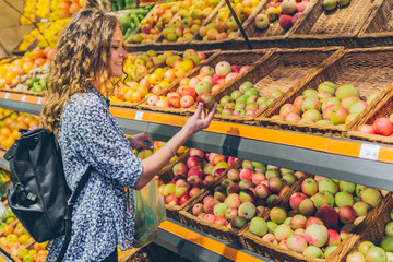 young adult woman choosing apples in grocery store