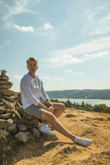 Naklejka na ściany i meble Male Model Sitting on a Stone Cairn Overlooking Lake