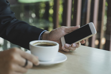 Closeup image of businessmen hands holding digital mobile with blank copy space screen for your text message or promotional content against desktop and coffee cup.