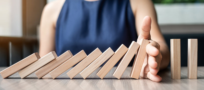 Businesswoman hand Stopping Falling wooden Dominoes. Business, Risk Management, Solution and strategy Concepts