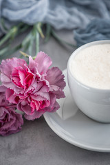 Cup of coffee cappuccino and pink carnation flowers on a gray background
