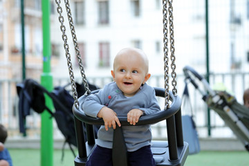 Cute Baby Boy Sitting On A Swing In Park