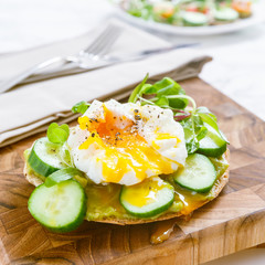 Raw healthy burger with avocado dressing, cucumbers, poached egg and multigrain bread. Superfood snack concept