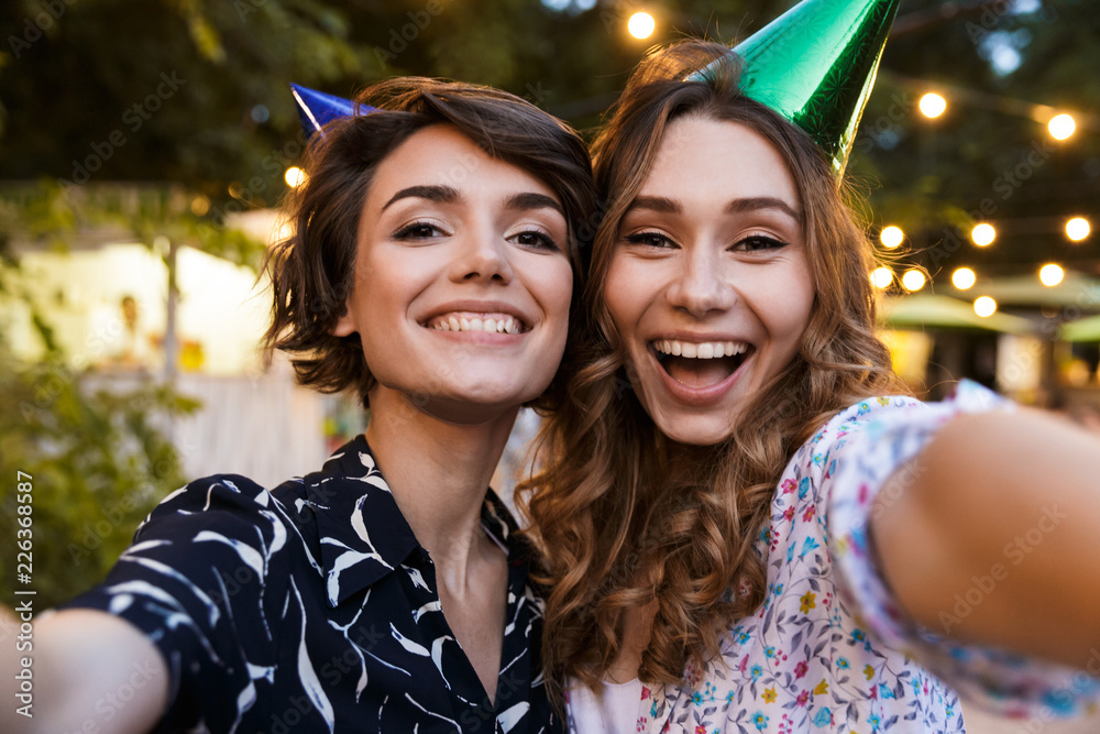 Wall mural Women friends outdoors in park having fun looking camera take a selfie.