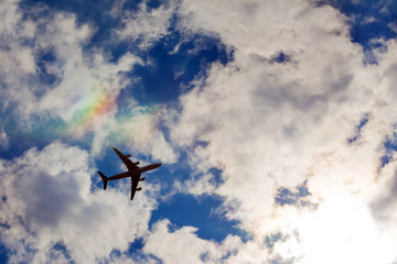 Airplane in the blue sky with white clouds, background. Rainbow against the sky