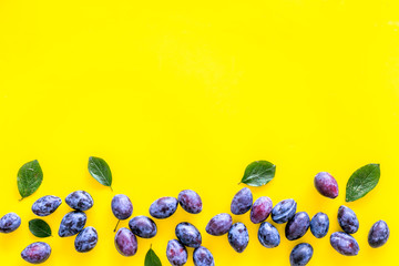 Blue plum for dessert. Purple plum and leaves pattern on yellow background top view copy space