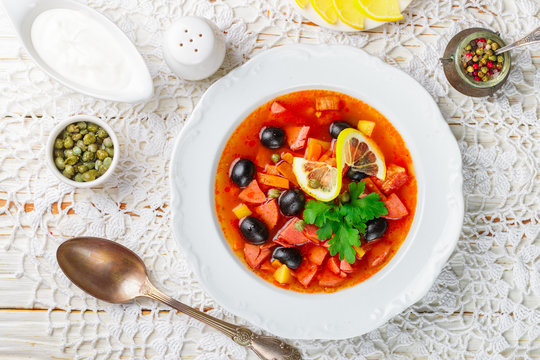 Traditional Russian soup Solyanka with meat, sausages, vegetables, capers, pickles and olives with lemon, seasonings and spices. Served with sour cream. Rustic style