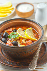 Traditional Russian soup Solyanka with meat, sausages, vegetables, capers, pickles and olives with lemon, seasonings and spices. Served with sour cream. Rustic style