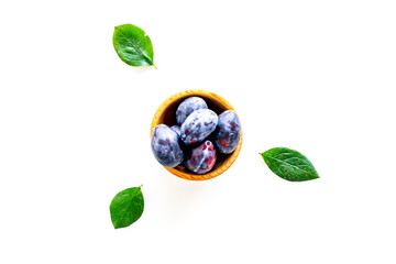 Plums on dinning table. Fresh raw purple plum in wooden bowl on white background top view space for text