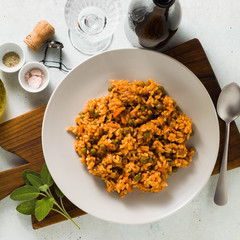 Italian risotto with tomato sauce and green peas, served in a plate on a wooden cutting board and a bottle of red sparkling wine . classic Mediterranean cuisine. healthy vegan meal 