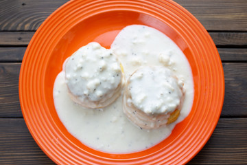 Two homemade biscuits smothered in sausage gravy set on an orange plate on the kitchen table for breakfast