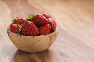 Ripe strawberries in wooden bowl on wood background with copy space