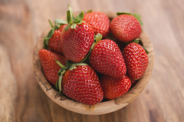 Ripe strawberries in wooden bowl on wood background from above