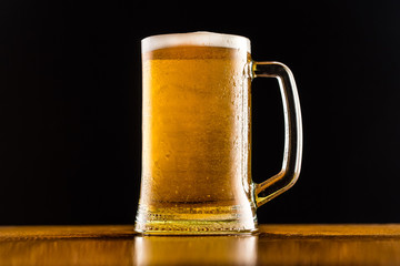 Frosty mug of beer close up on wooden table against black background.