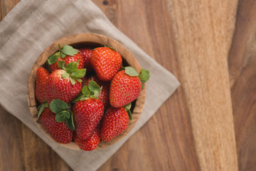 Ripe strawberries in wooden bowl on wood background with copy space top view