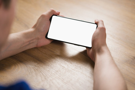 Young Man Hands Holding Smartphone With Blank White Screen In Landscape Mode