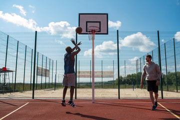 Full length portrait of two young men playing basketball in outdoor court, focus on African man...