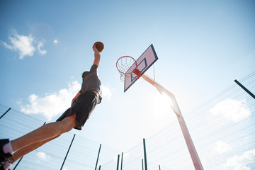 Wide angle portrait of young sportsman shooting slam dunk in basketball court outdoors, copy space