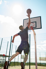 Full length portrait of young sportsman shooting slam dunk in basketball court outdoors, copy space