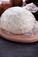 Fototapeta na wymiar Yeast dough with herbs on a wooden board surrounded by the ingredients