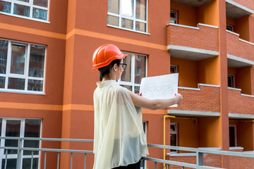 Woman in helmet comparing blueprint and built building