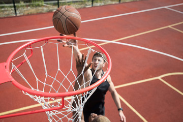 Obraz premium High angle portrait of young basketball player throwing ball in hoop and scoring on outdoor court lit by sunlight, copy space