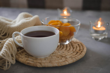 Fototapeta na wymiar Cup of tea and dried apricots on a table, candles and knited blanket.