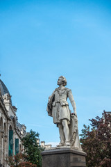 Fototapeta na wymiar Antwerp, Belgium - September 24, 2018: Gray statue of Sir Anthony Van Dyck Flemish Painter against blue sky at Meir and Leysstraat link. Facades and some green foliage.