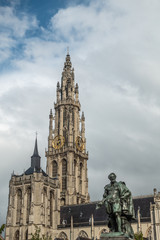 Fototapeta premium Antwerp, Belgium - September 24, 2018: Peter Paul Rubens bronze statue with towers of Onze-Lieve-Vrouwe Cathedral of Our Lady in back under white cloudy sky.