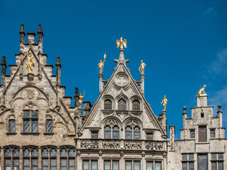 Fototapeta na wymiar Antwerp, Belgium - September 24, 2018: Golden statues on top of the facades of guild houses on Grote Markt. Brown stones, arches under blue sky.