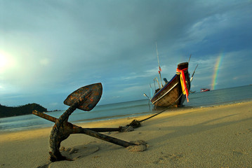 Long tail boat anchored on sand Thai beach against stormy sky with rainbow in background. Koh Pha...