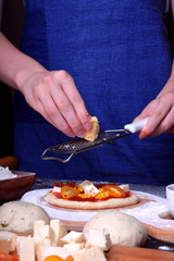 Process of making pizza. The cook wearing a blue apron is grating cheese