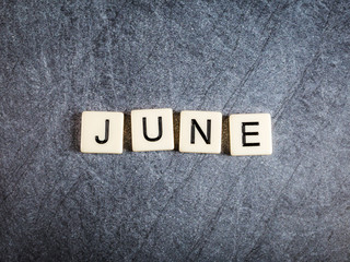 Letter tiles on black slate background spelling June