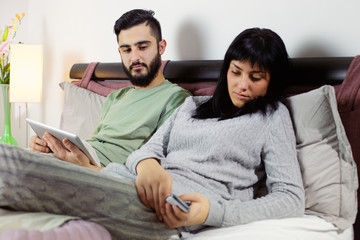 Man jealous of girlfriend looking her cell phone while she is chatting sitting in bed