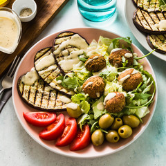 an appetizing dinner or lunch from a salad with tomatoes, grilled eggplants and legume falafel with sesame tahini dressing. Vegan healthy food for the whole family