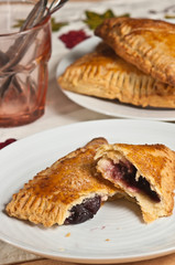 Front, top view, medium distance of three, freshly baked, homemade, cherry  cream turnovers and one ripped open to show cherry filling on a round white plate 