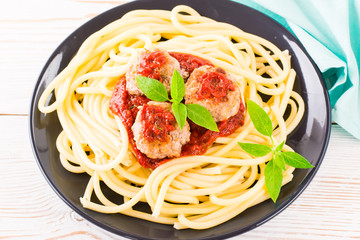 Close-up of spaghetti and meatballs in tomato sauce with fresh basil leaves on a plate