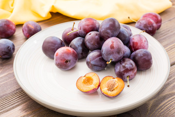 A broken ripe blue plum and whole berries on a plate on a wooden table