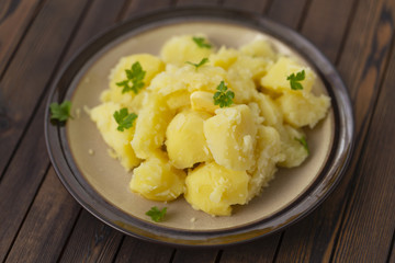 Boiled potatoes with fresh herbs and oil in a bowl on a wooden table