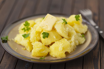 Boiled potatoes with fresh herbs and oil in a bowl on a wooden table