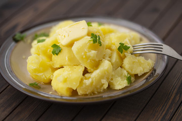 Boiled potatoes with fresh herbs and oil in a bowl on a wooden table