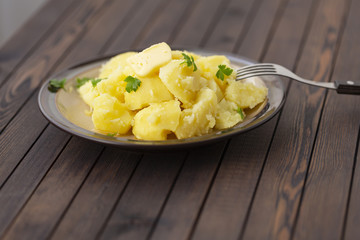 Boiled potatoes with fresh herbs and oil in a bowl on a wooden table
