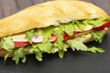 Baguette sandwich with ham, tomatoes, cheese and arugula lettuce. Delicious Breakfast or snack. Close up